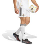 RMCFMP0301_04 | UAE SPORT STORE Lower body of a Real Madrid soccer player in white kit, holding a ball at the hip, wearing white socks with black stripes and black-red cleats.
