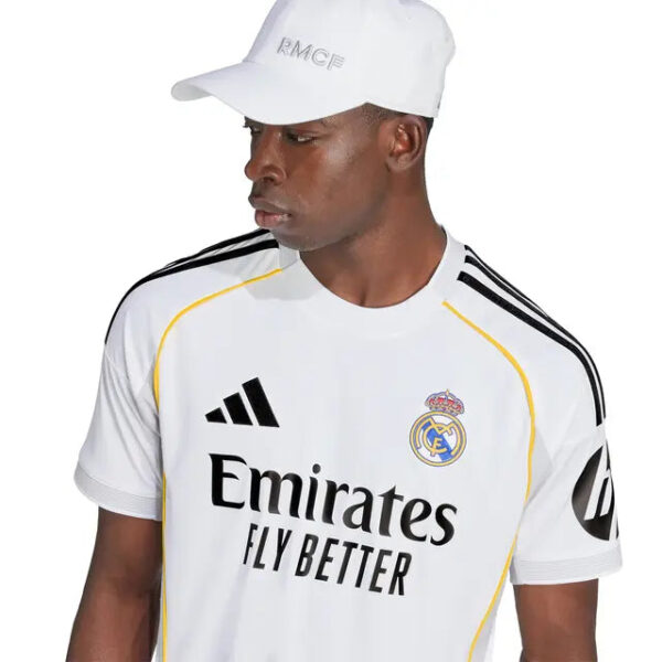 Man in a Real Madrid white football jersey with Emirates Fly Better logo, wearing a white cap, looking to the left.