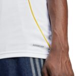 Close-up of a person wearing a white AEROREADY athletic shirt with a yellow seam and blue denim jeans with white stripes near the pocket area, arm visible.