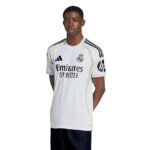 Man wearing a Real Madrid white football jersey with black and yellow accents, standing against a white background.