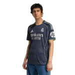 Male model wearing a navy Real Madrid football jersey with Emirates sponsor, standing against a white background.