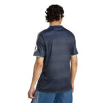 Back view of a man wearing a navy athletic jersey with short sleeves and light trim, paired with blue jeans on white background.