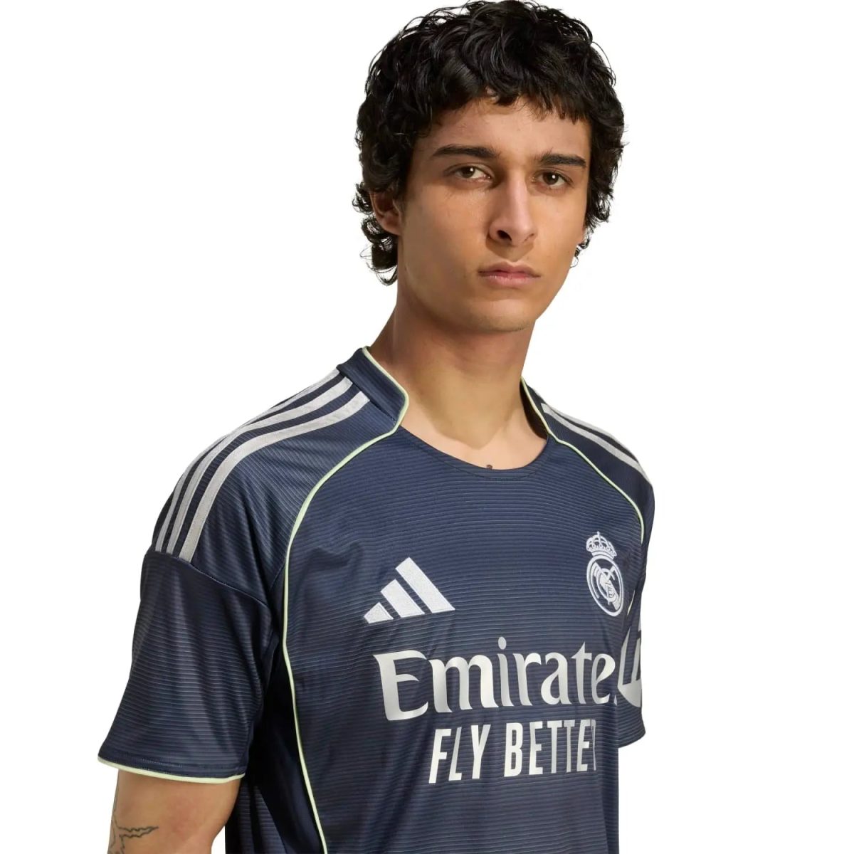 Young man in a Real Madrid jersey facing the camera with a neutral expression; sponsor text 'Emirates Fly Better' visible on the chest.