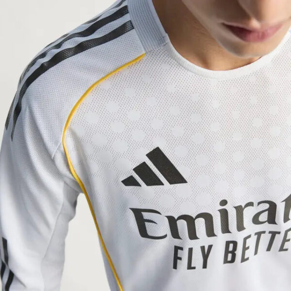 Close-up of a person wearing a white Adidas football jersey with black stripes and the 'Emirates Fly Better' logo.