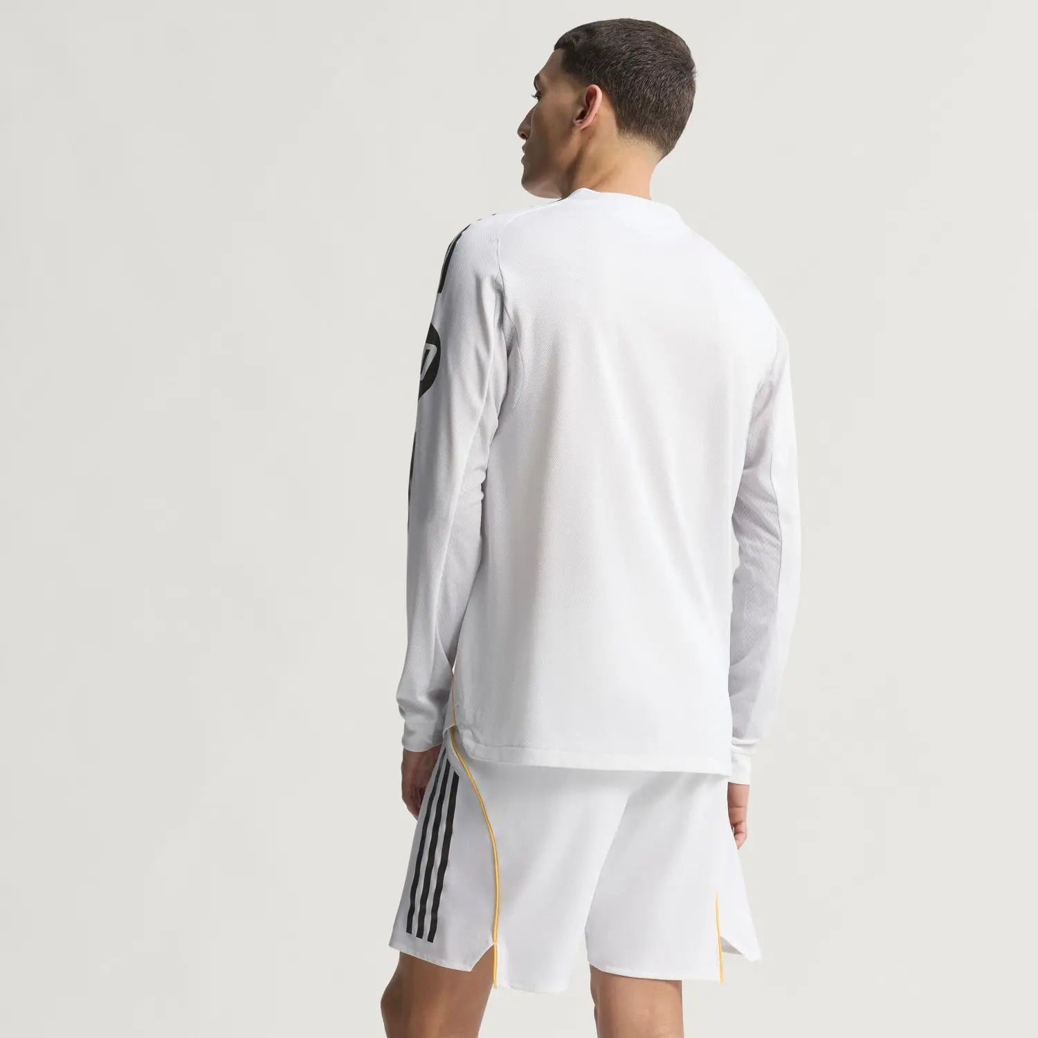 RMCFMZ0902_05 | UAE SPORT STORE Back view of a person in a white athletic long-sleeve shirt and white shorts with black side stripes and yellow trim.