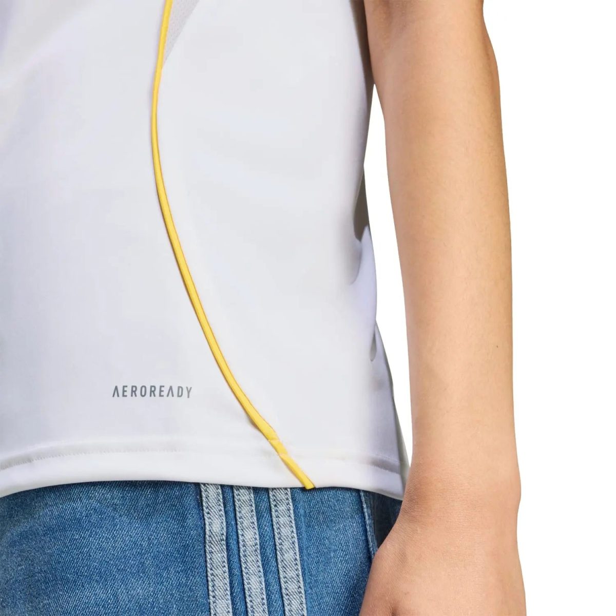 Close-up of a white athletic top with yellow piping, worn with blue jeans; 'AEROREADY' branding visible near the hem.