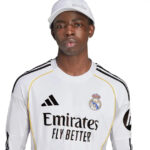 RMCFMZ0905_02 | UAE SPORT STORE Portrait of a young man wearing a Real Madrid white jersey with Emirates Fly Better logo and a white cap, looking straight ahead.