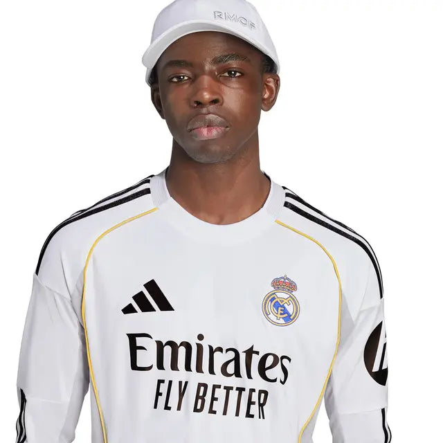 RMCFMZ0905_02 | UAE SPORT STORE Portrait of a young man wearing a Real Madrid white jersey with Emirates Fly Better logo and a white cap, looking straight ahead.