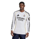 Male model wearing a white Real Madrid long-sleeve football jersey with black stripes and Emirates sponsor text, posed against a plain background.
