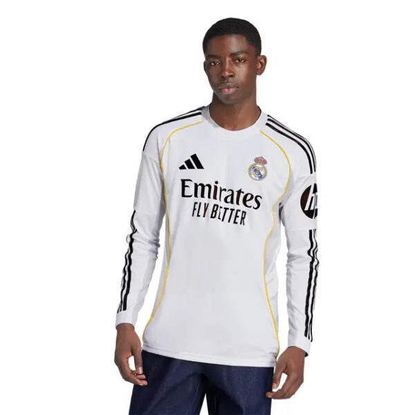 Male model wearing a white Real Madrid long-sleeve football jersey with black stripes and Emirates sponsor text, posed against a plain background.