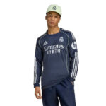 Man wearing Real Madrid navy training shirt with Emirates Fly Better logo and a light cap.