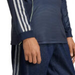Close-up of a person wearing a navy athletic jacket with white stripes on the sleeve and dark jeans.