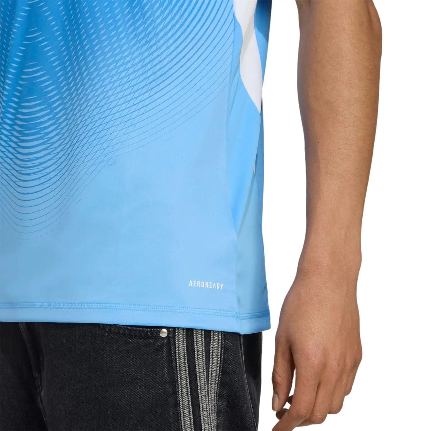 RMCFMZ0916_03 | UAE SPORT STORE Close-up of a light blue athletic shirt with diagonal wave pattern, hem visible, paired with dark jeans showing a vertical stripe detail.