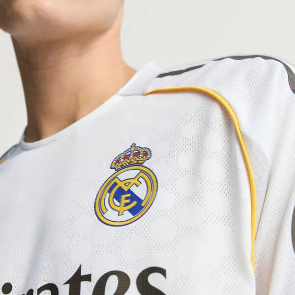 Close-up of a Real Madrid soccer jersey with the club crest on the chest and white fabric with subtle dots.