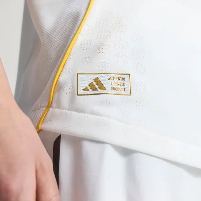 RMCFMZ0919_04 | UAE SPORT STORE Close-up of a white garment with yellow piping and a gold-bordered patch that reads 'AUTHENTIC LICENSED PRODUCT'.