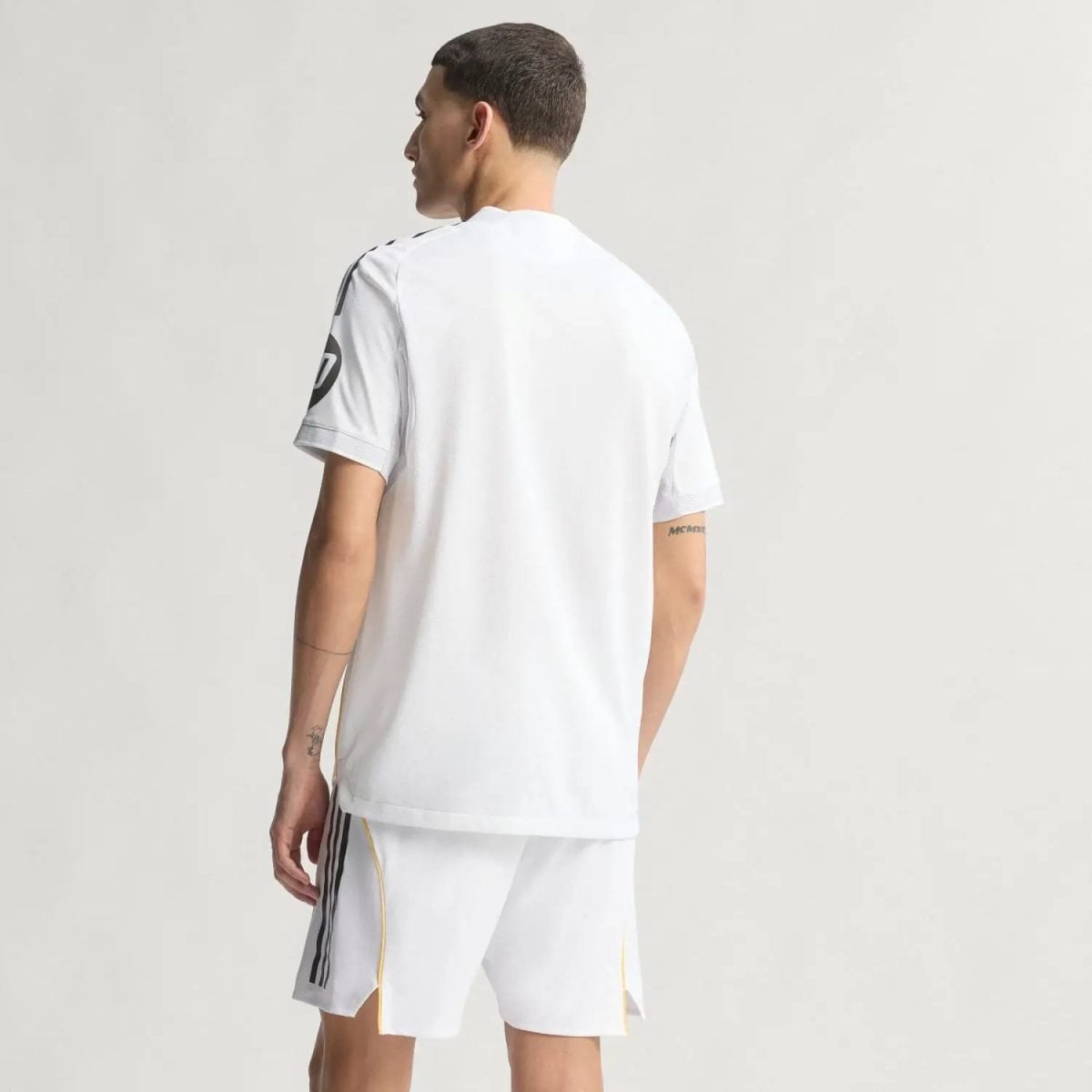 Back view of a man in a white athletic jersey and shorts, facing away, with dark side stripes on the shorts.