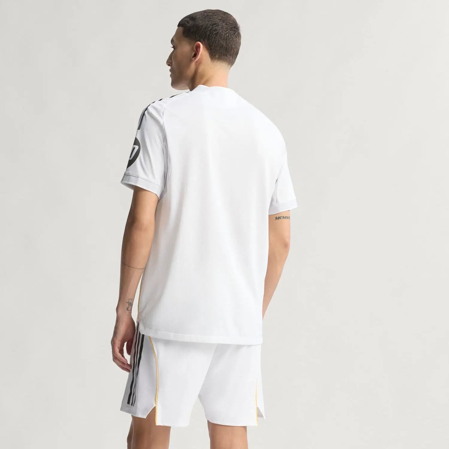 RMCFMZ0919_06 | UAE SPORT STORE Back view of a man in a white athletic jersey and shorts, facing away, with dark side stripes on the shorts.