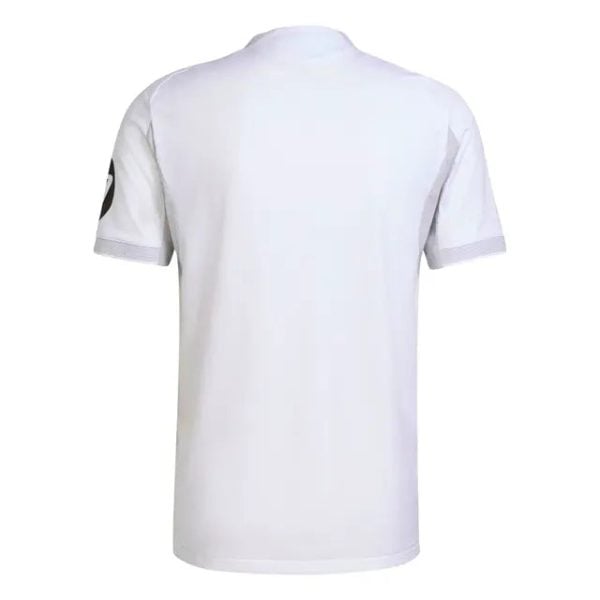 White short-sleeve polo shirt shown from the back, featuring a dark circular patch on the left sleeve.