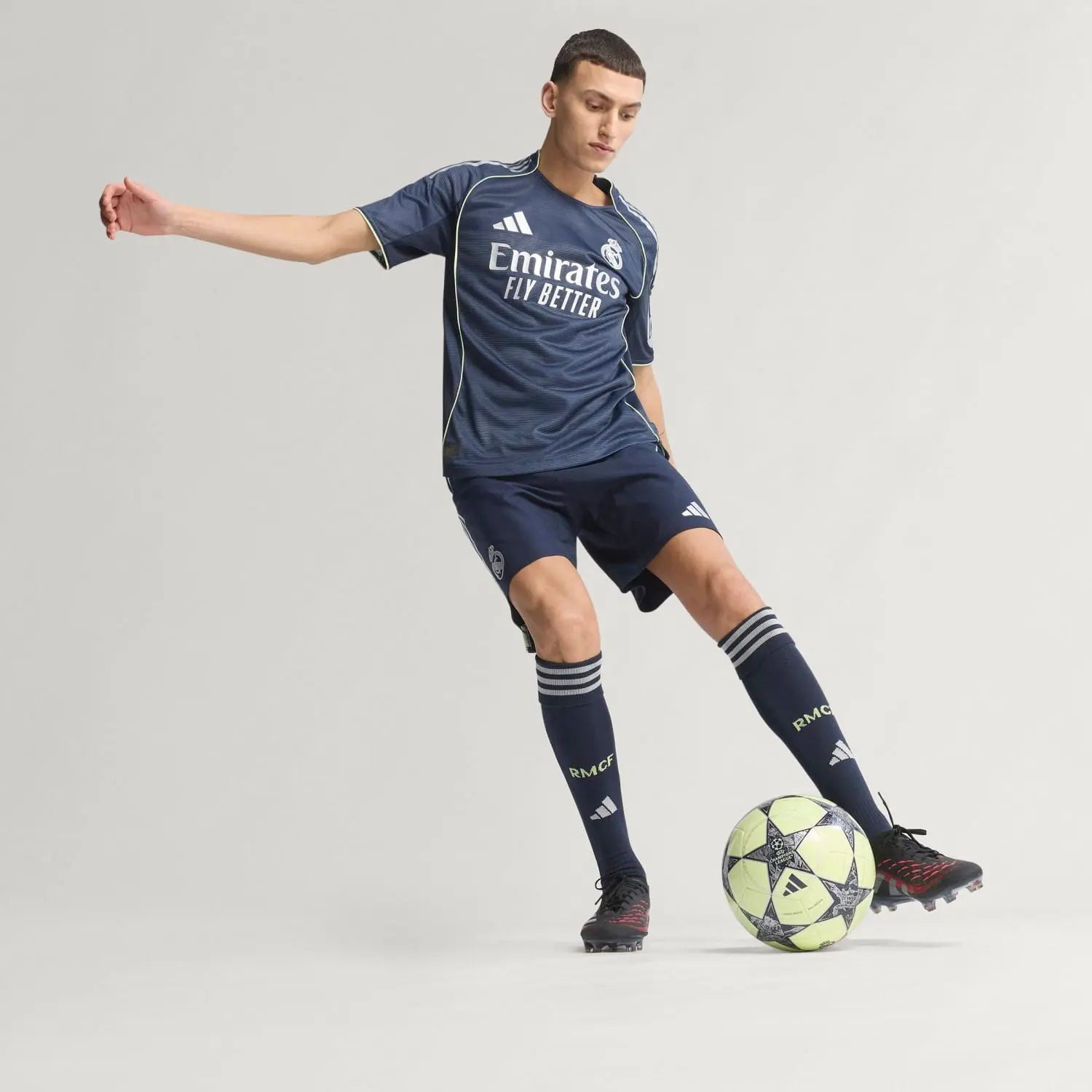 RMCFMZ0920_11 | UAE SPORT STORE Male soccer player in a navy Real Madrid kit dribbling a neon-yellow ball on a light background