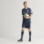 RMCFMZ0920_14 | UAE SPORT STORE Male model wearing a Real Madrid dark navy football kit holds a soccer ball while standing in a studio setting.