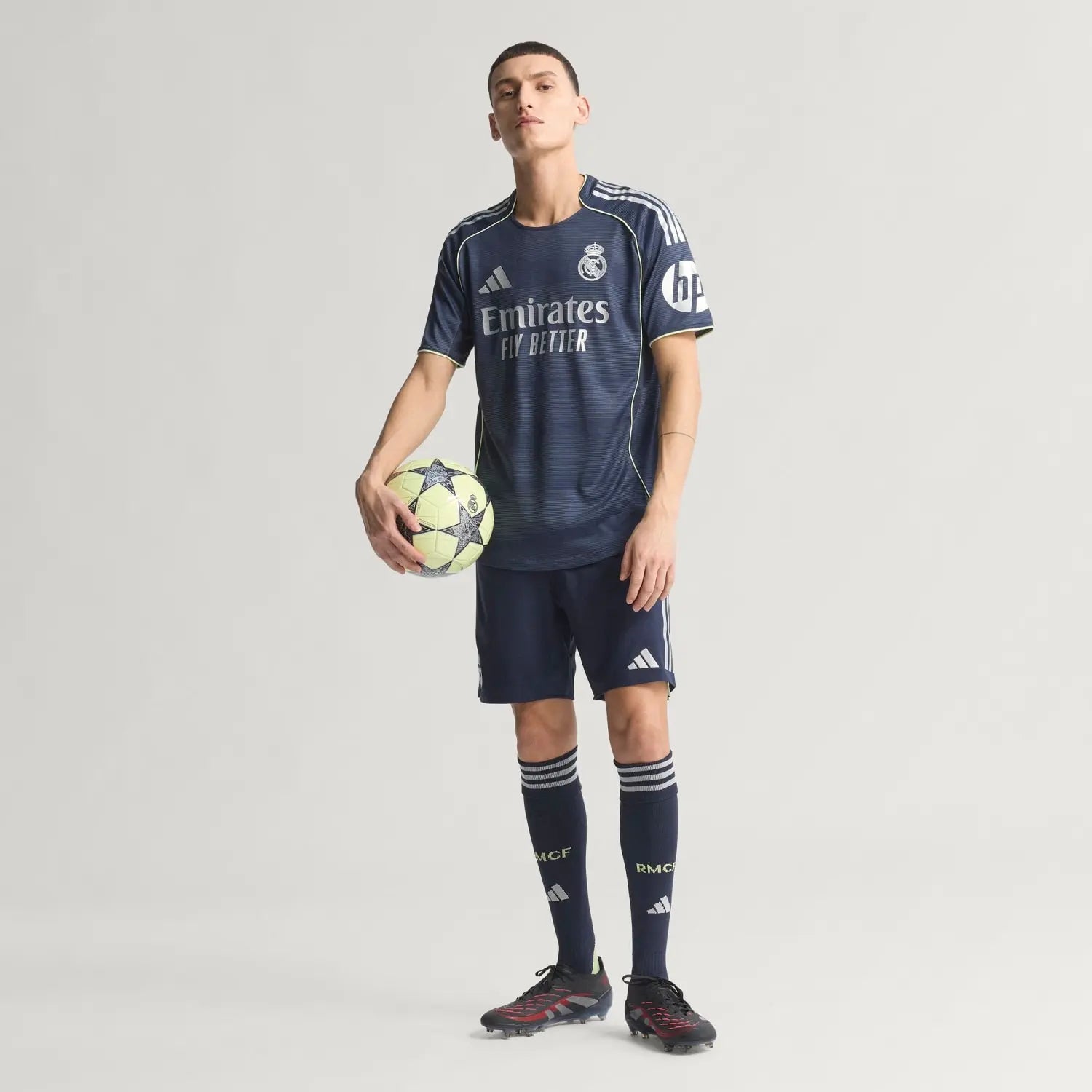 RMCFMZ0920_8 | UAE SPORT STORE Male soccer player in navy Real Madrid kit holding a ball, jersey reads Emirates Fly Better.