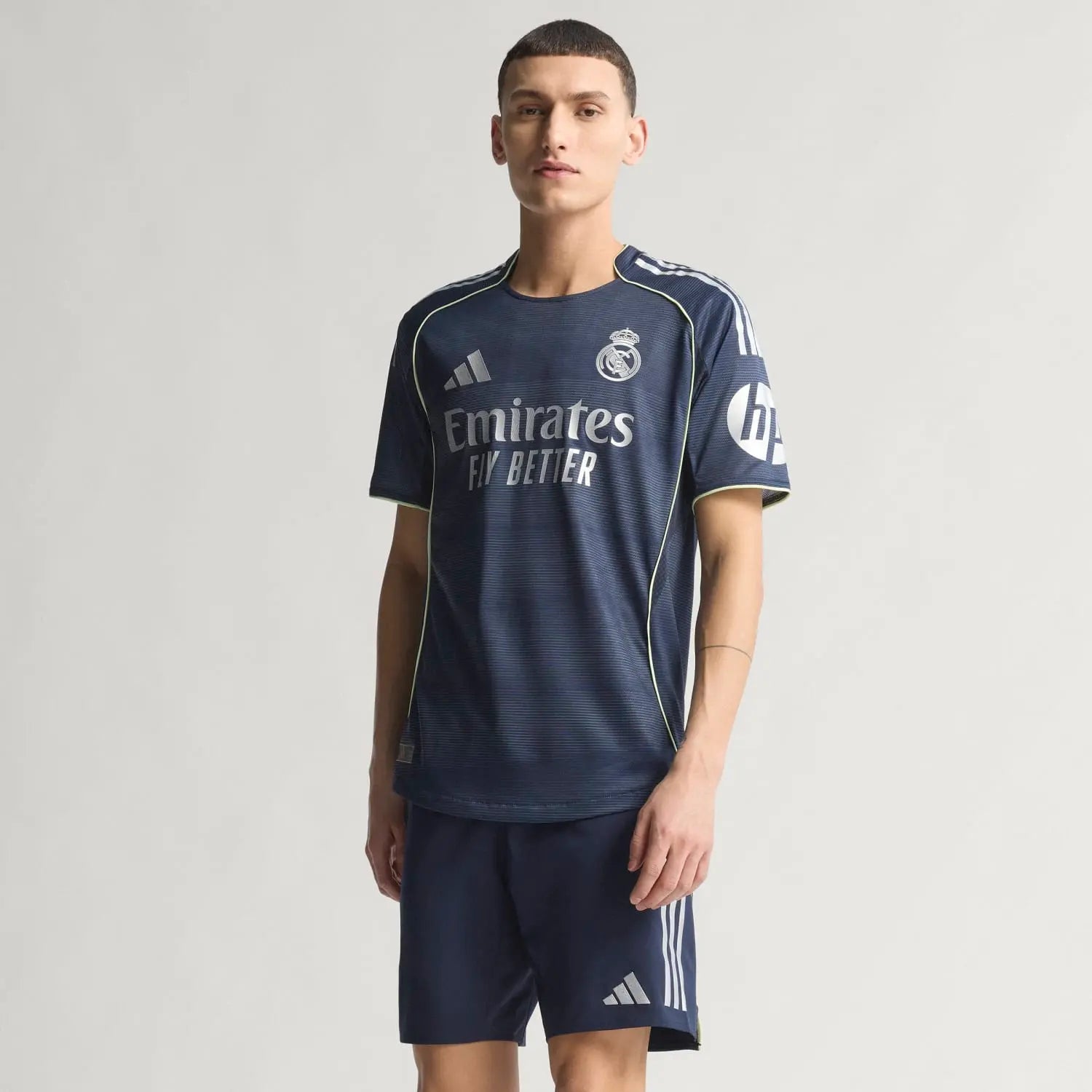 RMCFMZ0920_9 | UAE SPORT STORE Young man modeling a navy Real Madrid football jersey with Emirates Fly Better sponsor and HP logo on the sleeve against a light background.