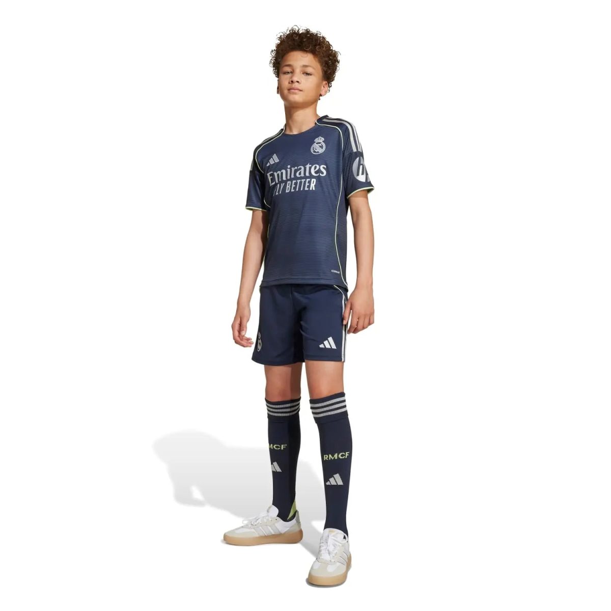 Young boy standing in a navy Real Madrid kids football kit, jersey and shorts, with matching socks and sneakers, sponsor logo visible.