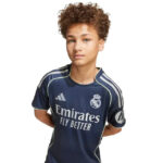Young boy with curly hair wearing a navy Real Madrid football jersey featuring the Emirates Fly Better sponsor logo on the front.