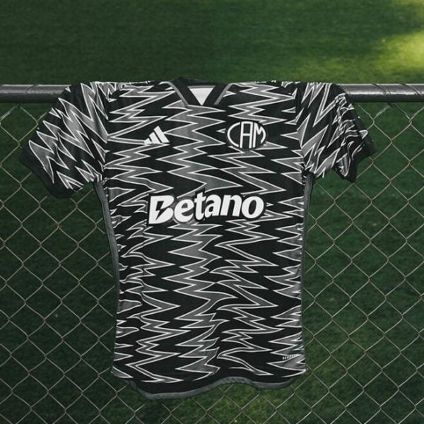 Black-and-white zigzag-patterned soccer jersey hanging over a chain-link fence with a Betano sponsor logo visible on the front.