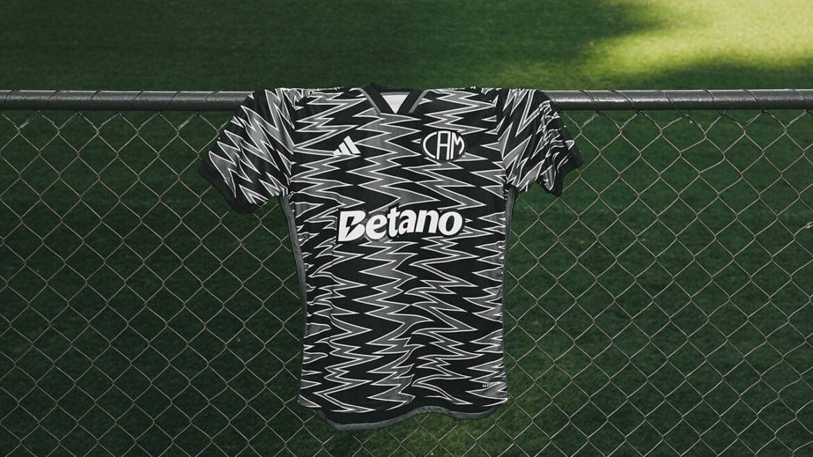RXZqRomvFRxSkG6 | UAE SPORT STORE Black-and-white zigzag-patterned soccer jersey hanging over a chain-link fence with a Betano sponsor logo visible on the front.