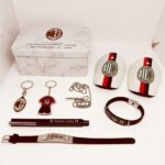 Layout of AC Milan memorabilia: marble-patterned box, two logo badges, keychains, bracelet, necklace, pen, and belt laid out on a white surface.