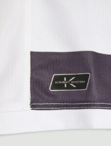 Close-up of white fabric with a dark purple stitched patch displaying the KOMBAT SYSTEM logo.