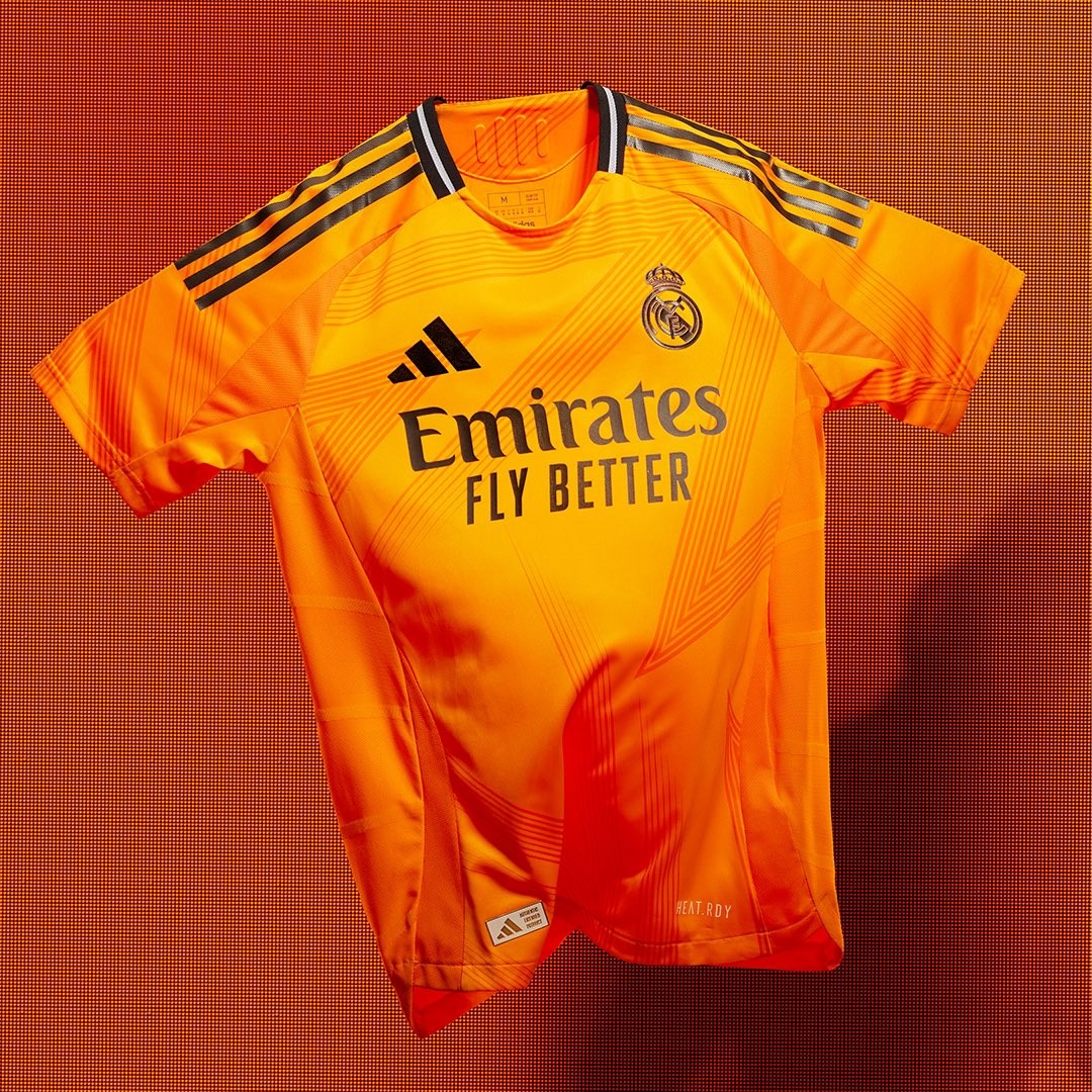 Rdwqv1eoxejVNVD | UAE SPORT STORE Bright orange Real Madrid football jersey with Emirates Fly Better sponsor, club crest, and Adidas stripes on the shoulders, displayed against a matching orange background.