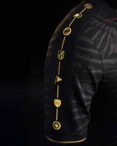 RightSleeve_3000x_7a6b448d-dc28-43e3-85b7-75261069b3a3 | UAE SPORT STORE Close-up of black jacket sleeve with vertical gold embroidery of circular symbols on a dark patterned fabric against a black background.