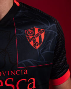 Close-up of a dark navy SD Huesca soccer jersey with a red crest and red trim.