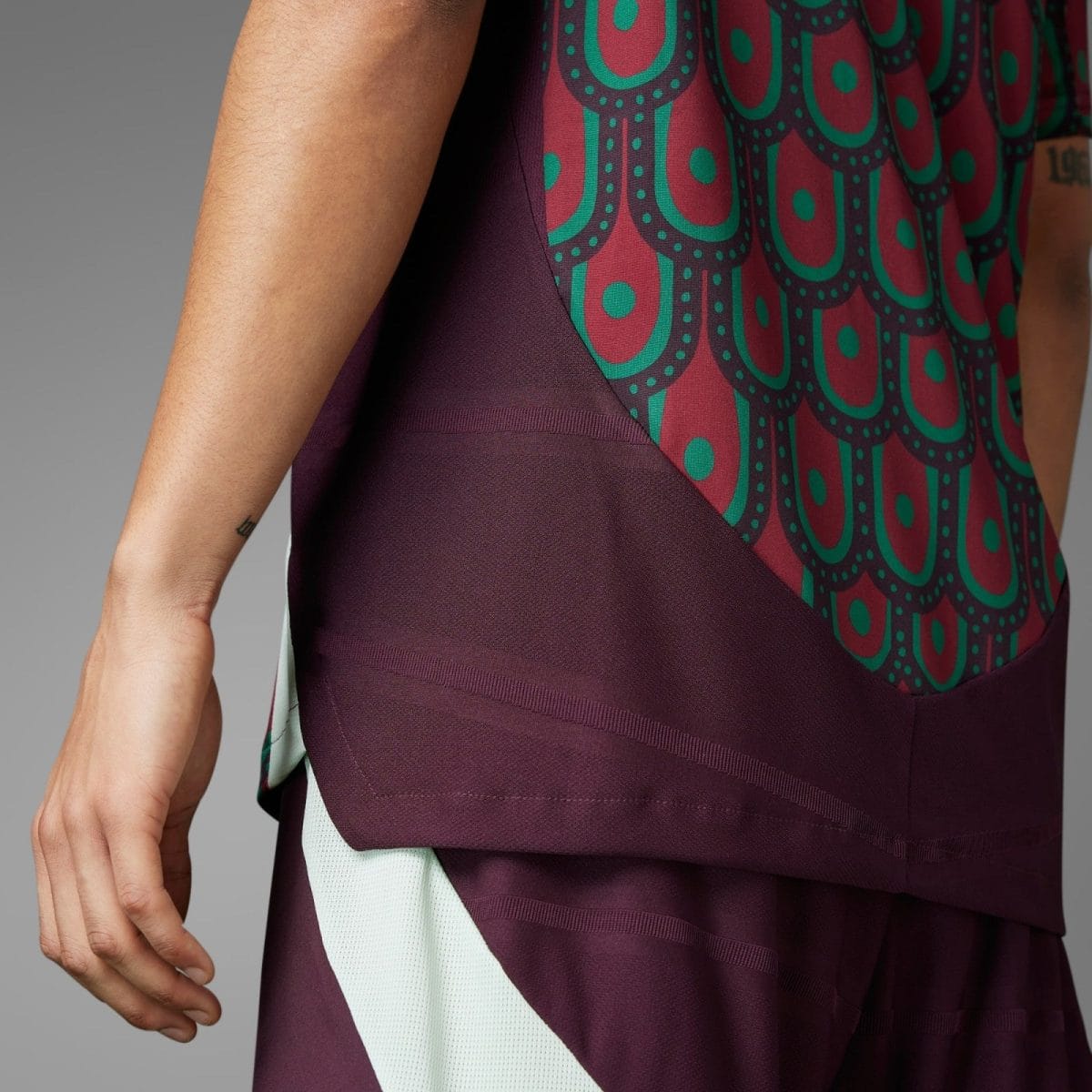 Close-up of a person’s arm beside a burgundy dress with teal circular pattern and a mint lining at the hem.