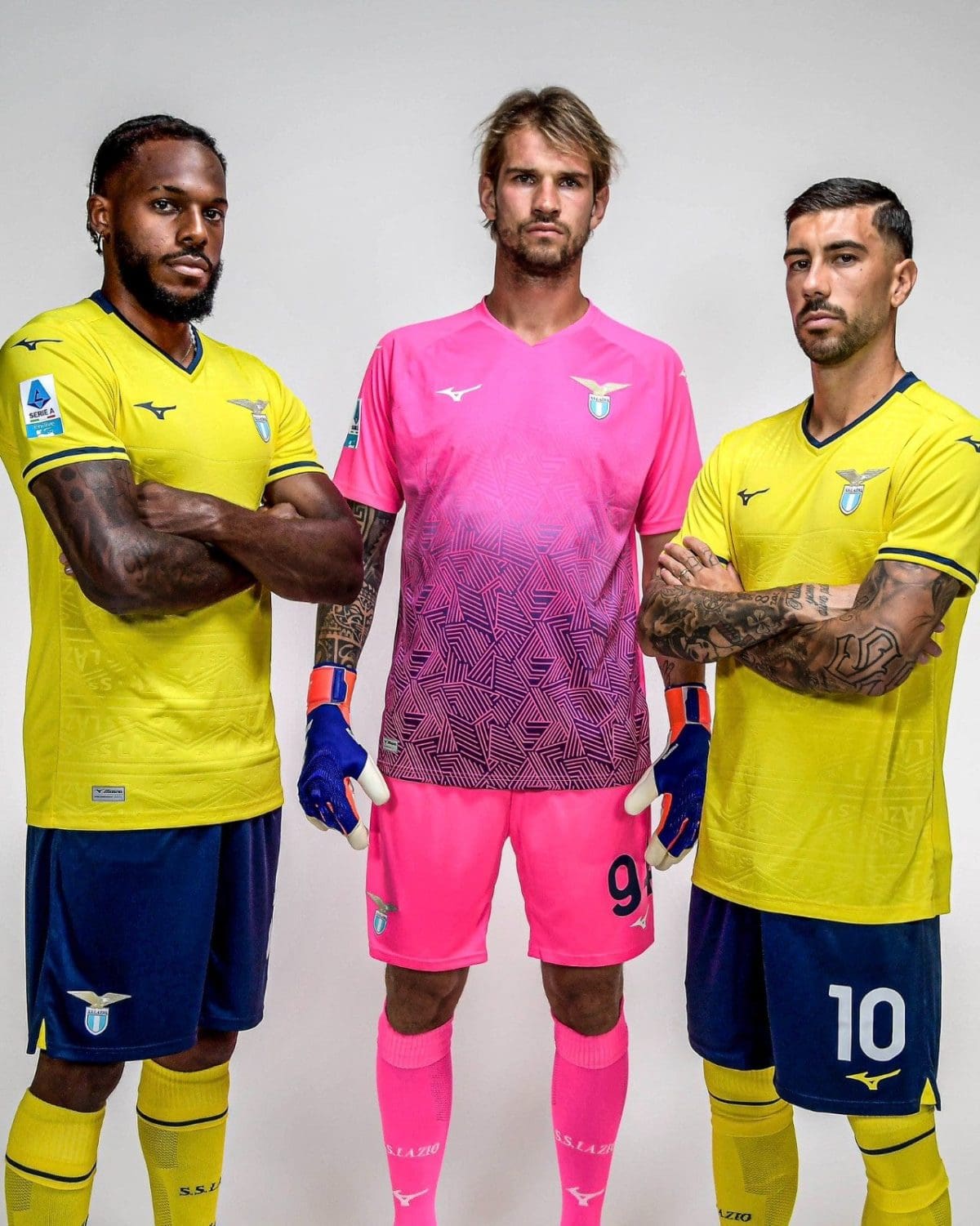 Three male soccer players pose together, two in yellow jerseys flanking a pink-clad goalkeeper in the center.