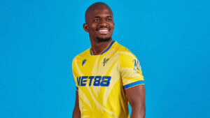 Smiling man in a yellow sports jersey against a solid blue background.