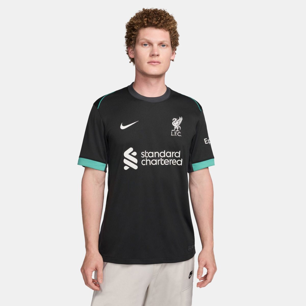 Front view of a person wearing a black Liverpool FC training jersey with teal trim, featuring the club crest, Nike swoosh, and 'standard chartered' sponsor logo on the chest.