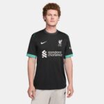SSS2-NKFN8780_322_196976453442_1_7410c3eb-103a-4b28-819e-8a2aa077b768 | UAE SPORT STORE Front view of a person wearing a black Liverpool FC training jersey with teal trim, featuring the club crest, Nike swoosh, and 'standard chartered' sponsor logo on the chest.