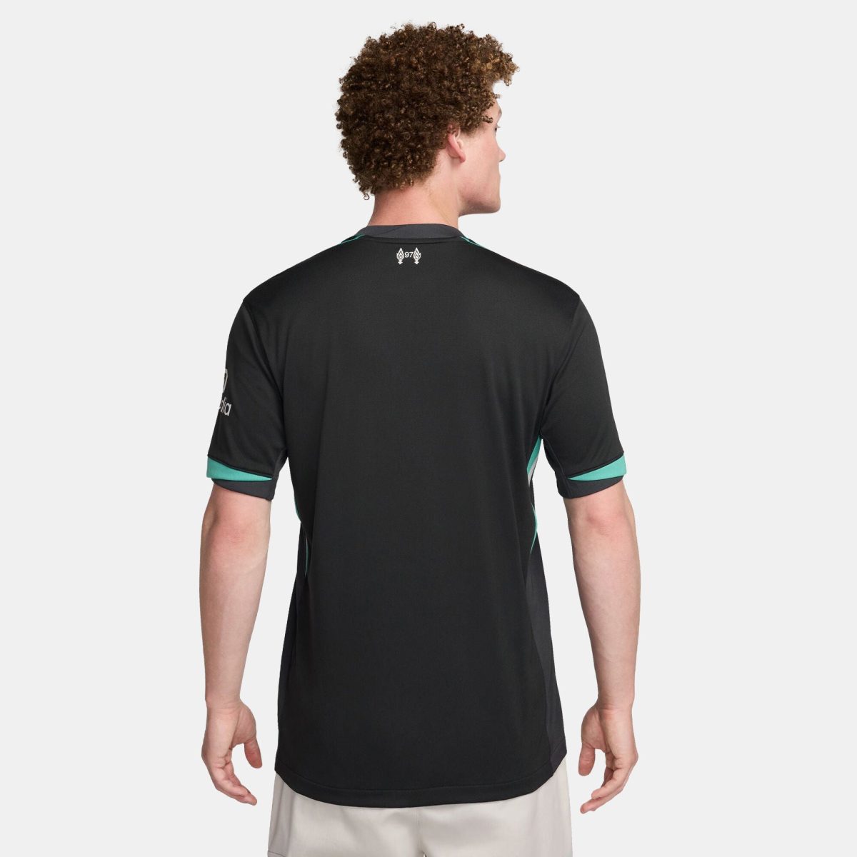 Back view of a person wearing a black athletic jersey with teal trim on the sleeves and a small white logo at the upper back against a light-gray background.