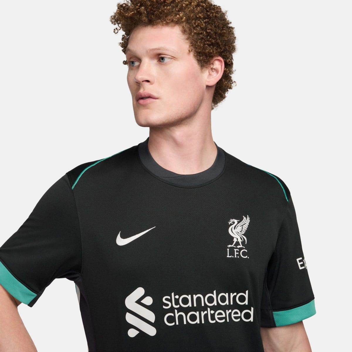Young man wearing a black Liverpool FC jersey with Nike swoosh and sponsor logo, shown from chest up, facing left.