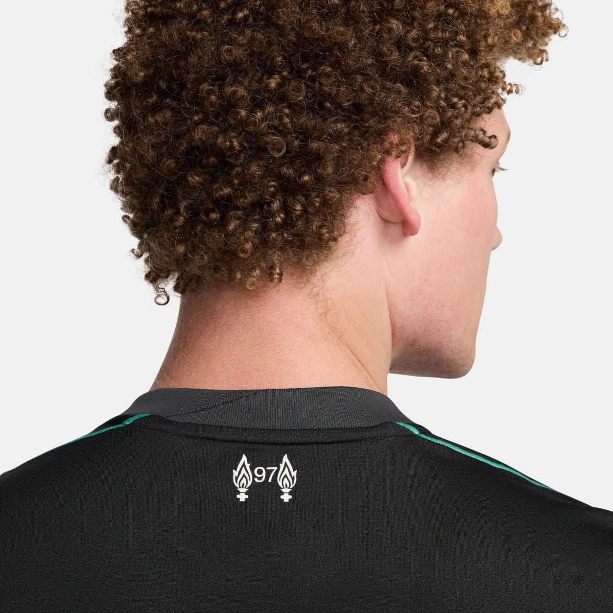 Rear view of a person with tight brown curls, wearing a black athletic shirt with teal trim and a white flame emblem on the back.