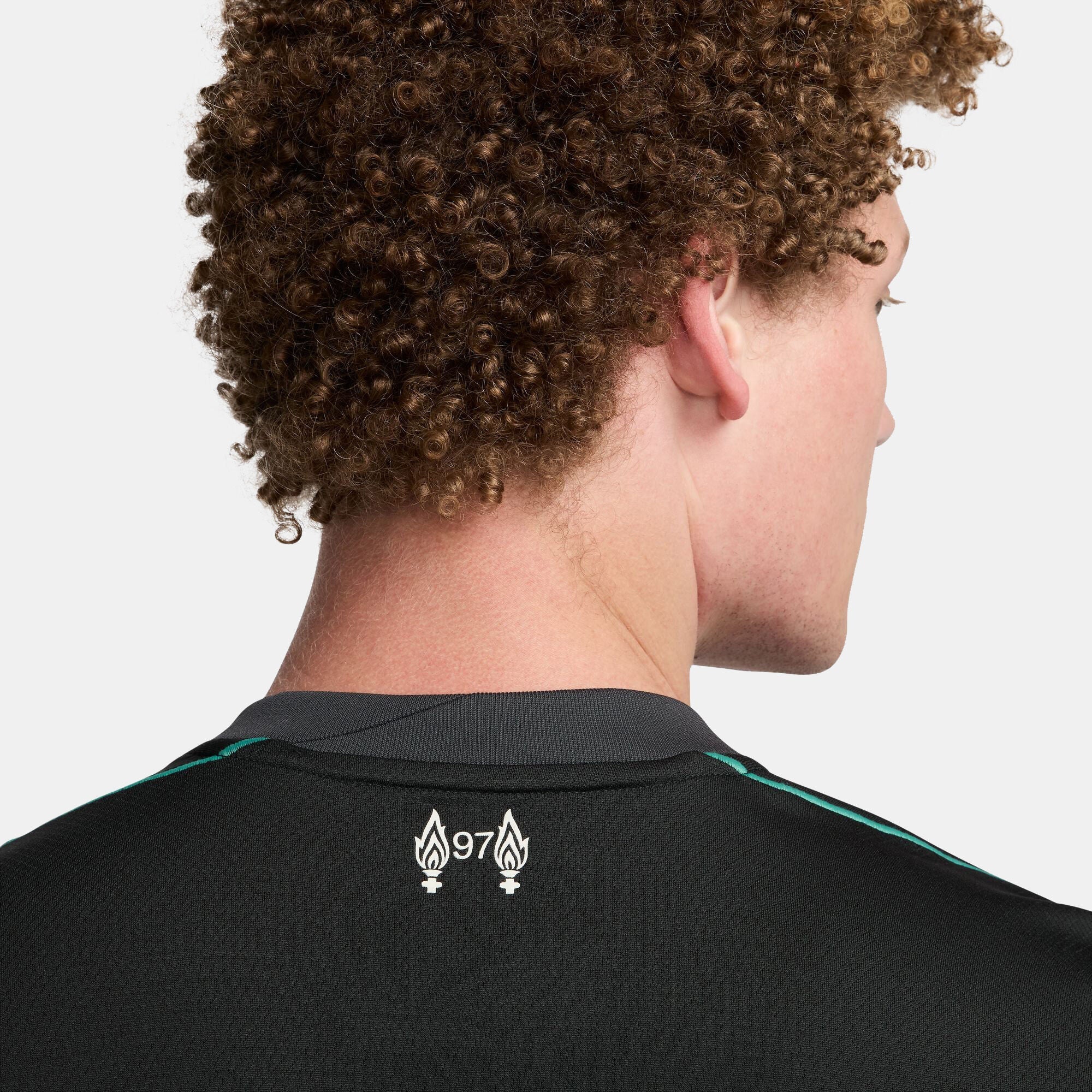 SSS2-NKFN8780_322_196976453442_6_e4c8cc25-b827-427c-bcfc-d43bf0b12c32 | UAE SPORT STORE Rear view of a person with tight brown curls, wearing a black athletic shirt with teal trim and a white flame emblem on the back.