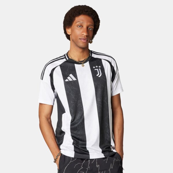 Person wearing a black-and-white striped soccer jersey, facing camera, with gold chain necklace and earring.