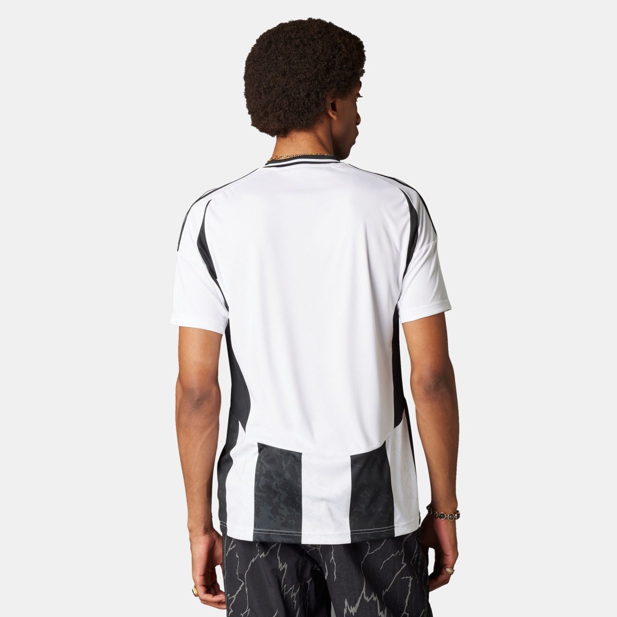 Person shown from behind wearing a white sports shirt with black trim and a gold chain necklace