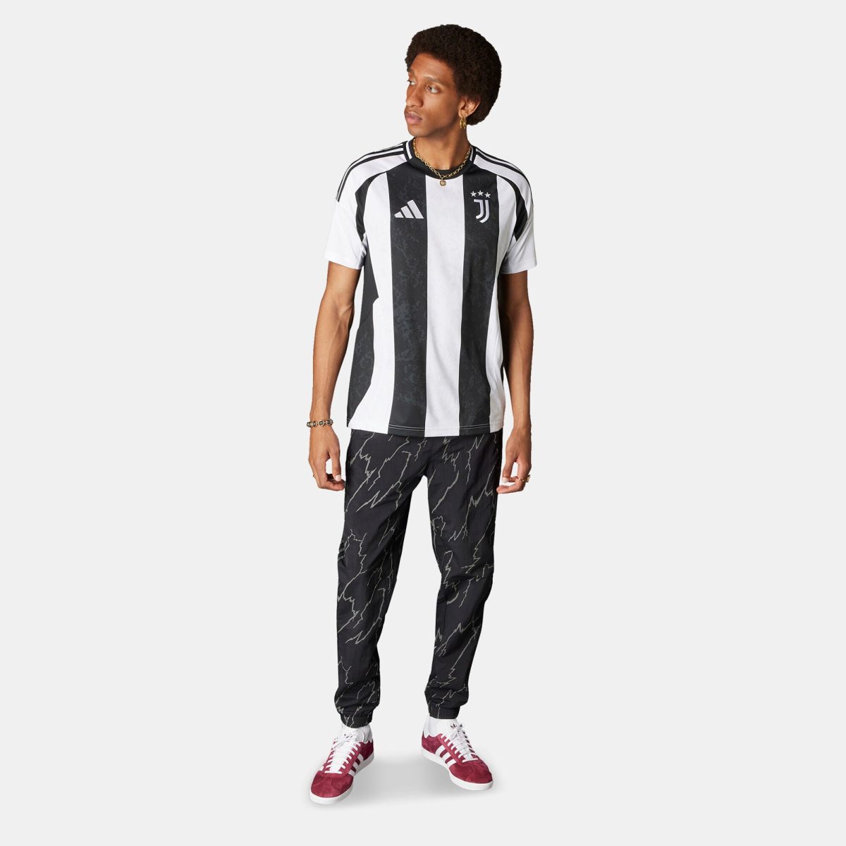Man wearing a black-and-white vertical striped Juventus soccer jersey with white sleeves, paired with dark pants and red sneakers, looking to the left.