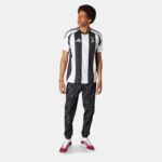 Man wearing a black-and-white vertical striped Juventus soccer jersey with white sleeves, paired with dark pants and red sneakers, looking to the left.