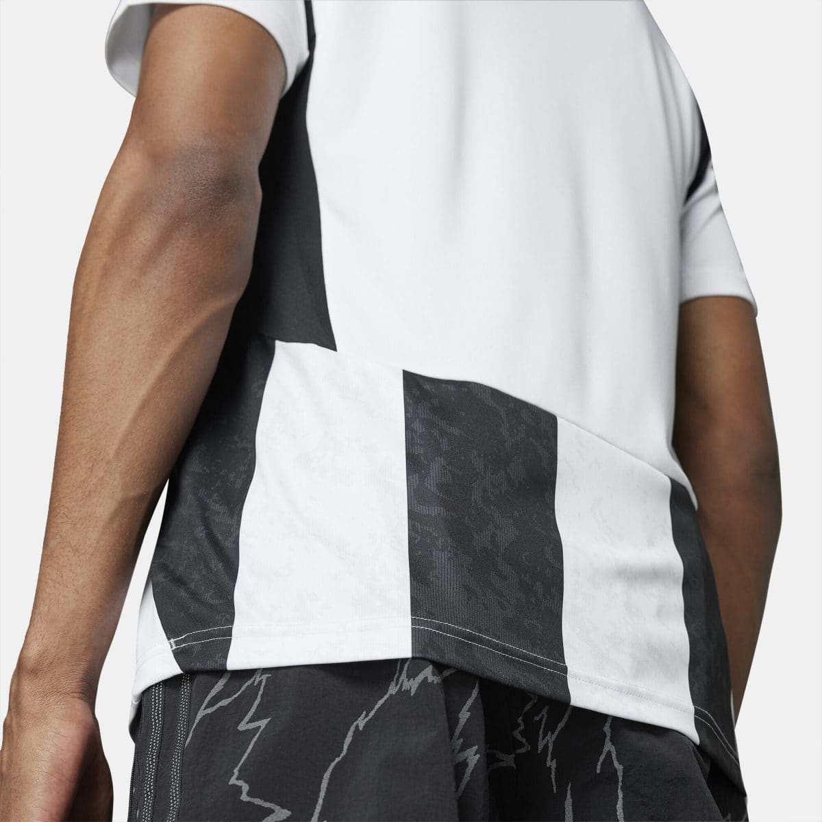 Close-up of a person’s arm and torso wearing a white garment with bold black vertical stripes; part of a patterned outfit is visible.