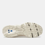 Bottom view of a white/cream New Balance sneaker outsole showing traction lugs and blue heel inserts.